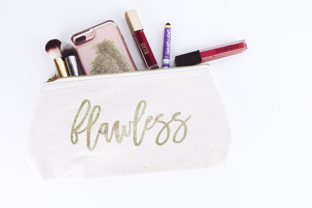 open makeup bag that says "flawless" containing various makeup products and a cell phone