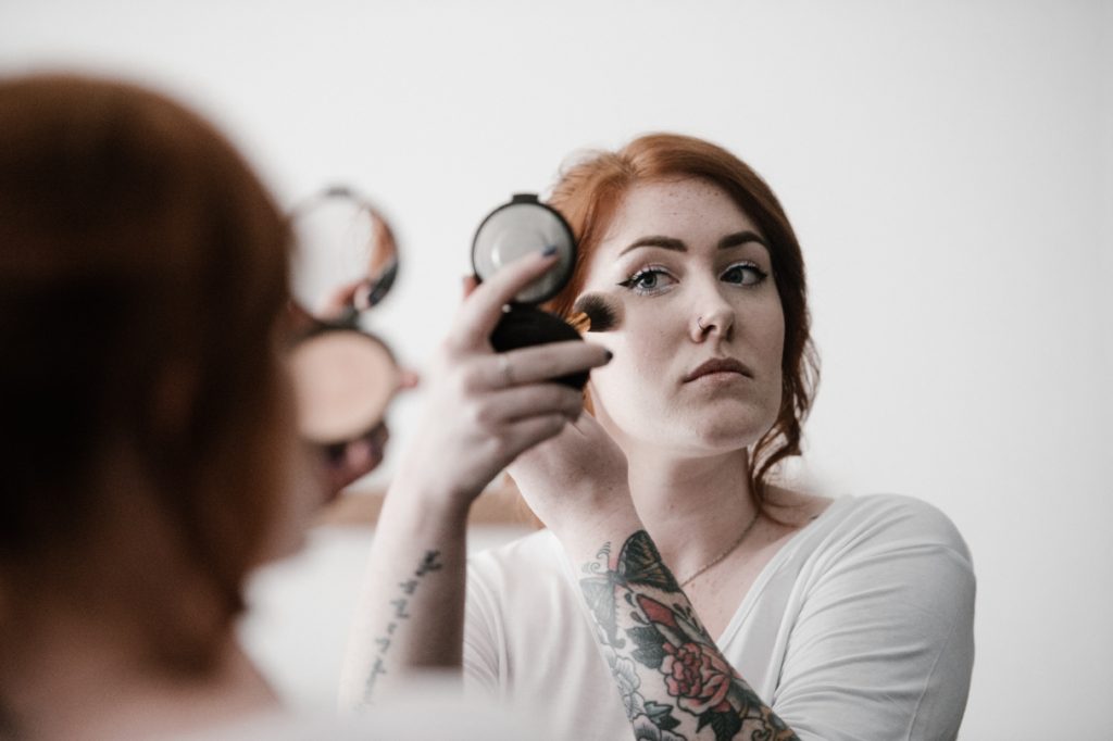 woman applying face powder with a brush while looking in mirror